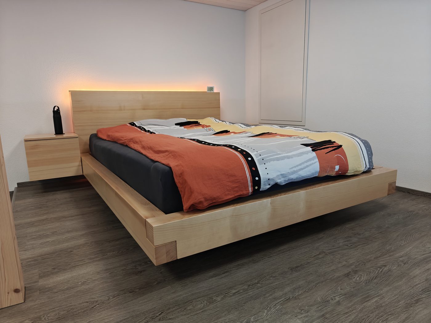 Schwebendes Bettsystem in Massivfichte — Frontalansicht mit Kopfteil, LED-Beleuchtung und Nachttisch